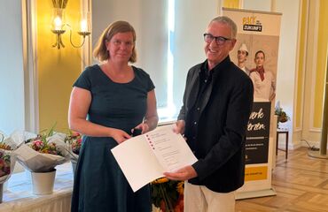 Hans-Hermann Schröer erhält den Ehrenbrief des Landes Hessen aus den Händen von Stadträtin Frau Löbcke. Die Verleihung findet in feierlichem Rahmen mit Blumen und Roll-up im Hintergrund statt.