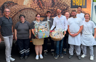 Gruppenfoto der Verabschiedung von Herrn Einbrodt vor einem Backhaus-Schröer-Fahrzeug. Gemeinsam mit der Geschäftsführung und Kolleginnen und Kollegen hält Herr Einbrodt Abschiedsgeschenke in den Händen.